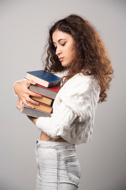 Jonge vrouw die bij een stapel boeken op een grijze muur toont. Hoge kwaliteit foto