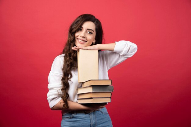 Jonge vrouw die boeken draagt en op een rode achtergrond glimlacht. Hoge kwaliteit foto