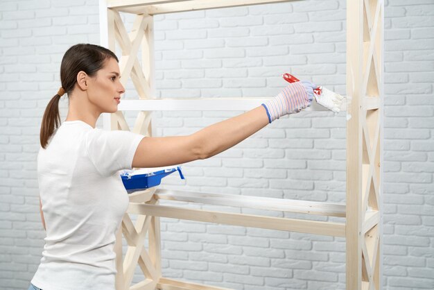 Jonge vrouw die borstel en witte kleur gebruikt voor het schilderen van rek