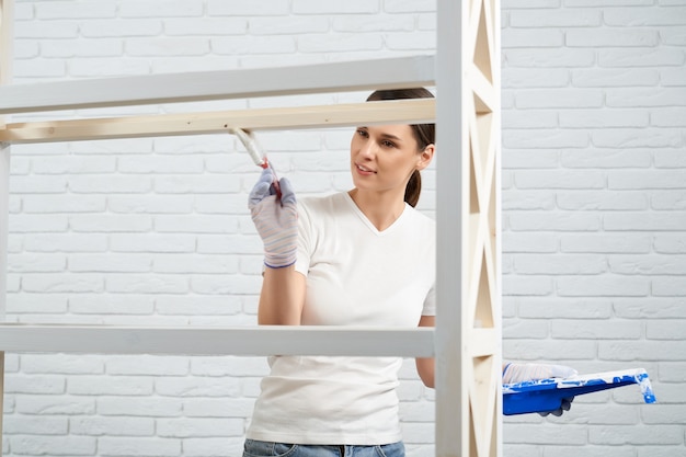 Gratis foto jonge vrouw die borstel en witte kleur gebruikt voor het schilderen van rek