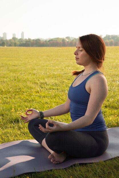 Jonge vrouw die buiten op yogamat mediteert