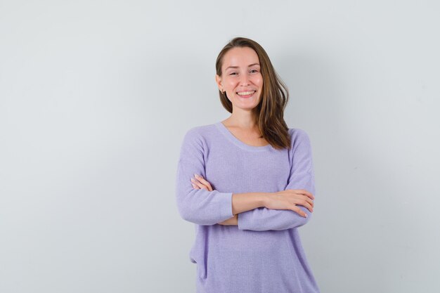 Jonge vrouw die de armen gekruist houdt terwijl ze in lila blouse glimlacht en er helder uitziet