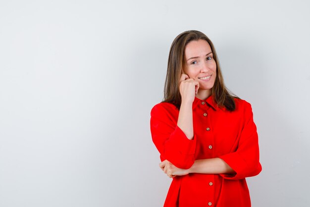 Jonge vrouw die de hand op de wang houdt in een rode blouse en er vrolijk uitziet, vooraanzicht.