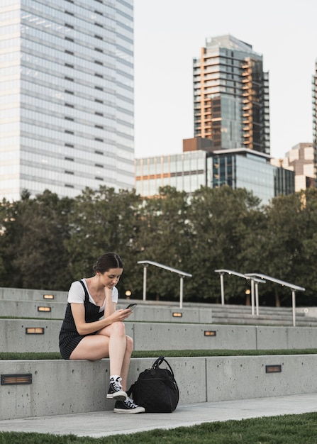 Gratis foto jonge vrouw die de telefoon in het park bekijkt