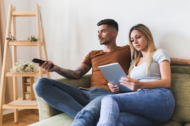 Jonge vrouw die digitale tabletzitting bekijkt met de mens het letten op televisie