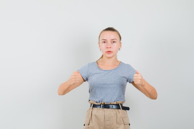 Jonge vrouw die doet alsof ze iets in een t-shirt, broek vasthoudt en zelfverzekerd kijkt, vooraanzicht.