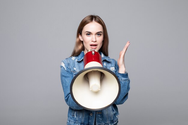 Jonge vrouw die door een megafoon schreeuwt om iets aan te kondigen dat op grijze muur wordt geïsoleerd