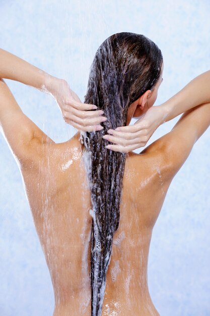 Jonge vrouw die douche neemt en haar haar wast - achteraanzicht