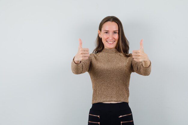 Jonge vrouw die duim in gouden blouse toont en blij kijkt