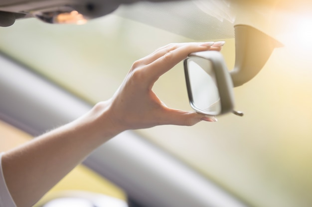 Jonge vrouw die een achteruitkijkspiegel in de auto aanpast