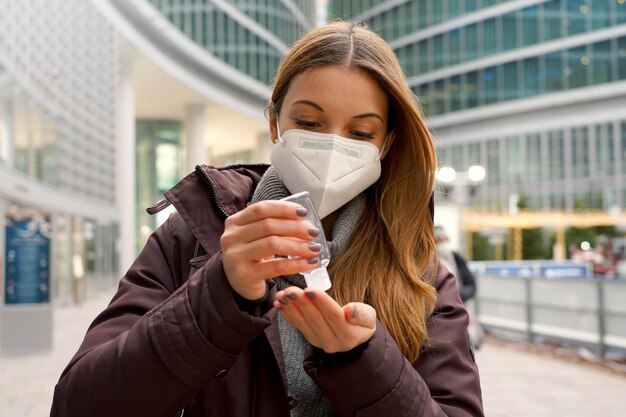 Jonge vrouw die een beschermend medisch masker draagt dat alcoholgel gebruikt die haar handen buiten het winkelcentrum desinfecteert. hygiëne en gezondheidszorg concept.