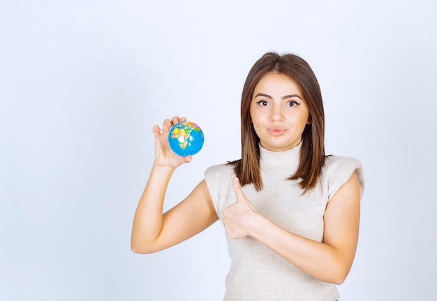 Jonge vrouw die een bol van de aardebol houdt en een duim toont.