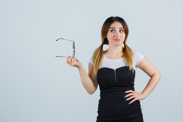 Jonge vrouw die een bril vasthoudt terwijl ze haar hand op de heup houdt