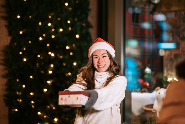 Jonge vrouw die een doos voor je geeft buiten in de winterstraat Geschenkuitwisselingsconcept.