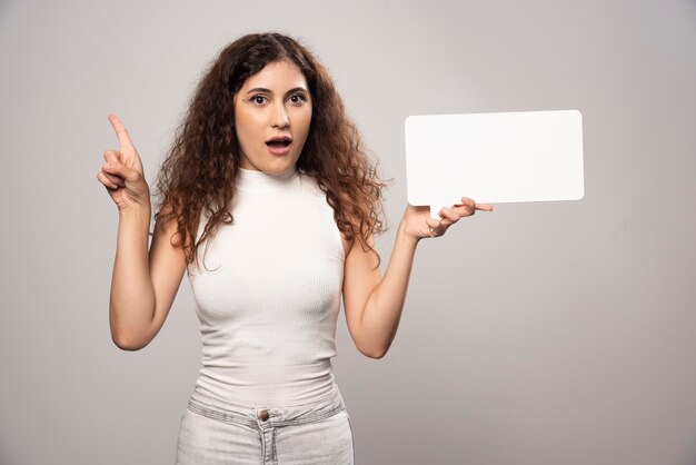 Jonge vrouw die een duim toont en lege witte affiche houdt. Hoge kwaliteit foto