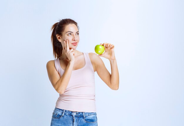 Jonge vrouw die een groene appel vasthoudt en denkt