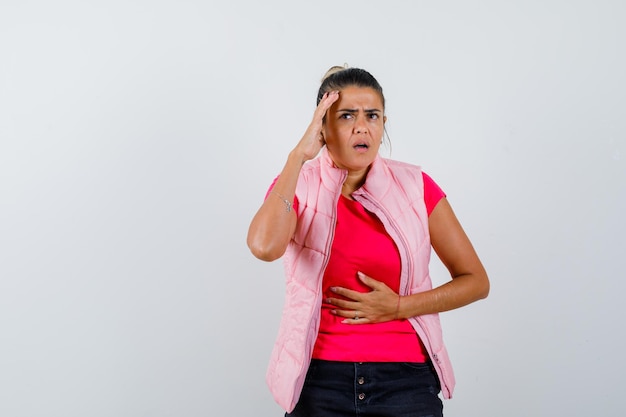 Jonge vrouw die een hand op de buik legt, een andere hand in roze t-shirt en jasje en er gehaast uitziet