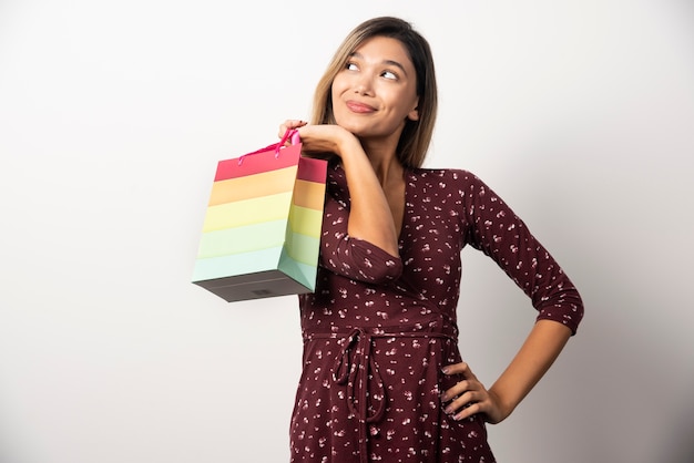 Jonge vrouw die een kleine winkeltas op witte muur houdt.