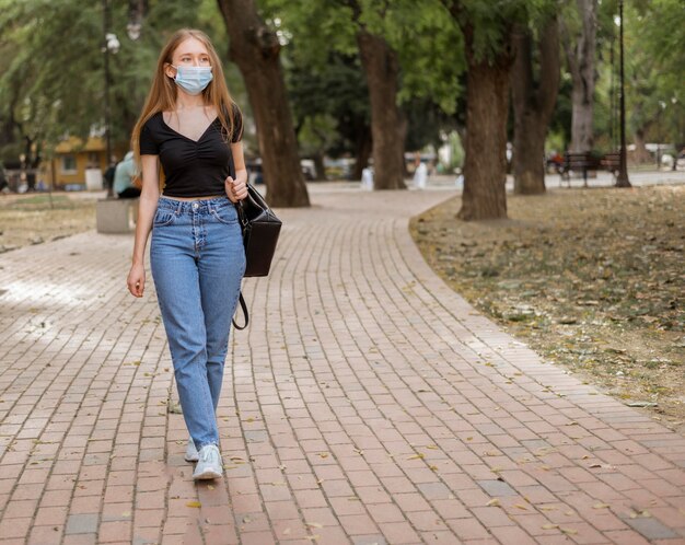 Jonge vrouw die een wandeling heeft terwijl ze een medisch masker draagt