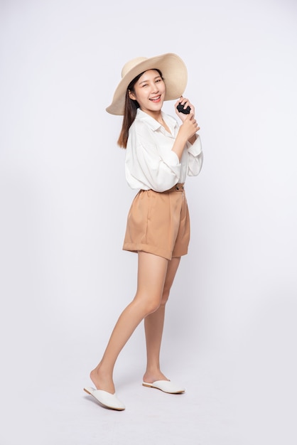 Jonge vrouw die een wit overhemd en korte broek draagt, een hoed draagt en een handvat op de hoed