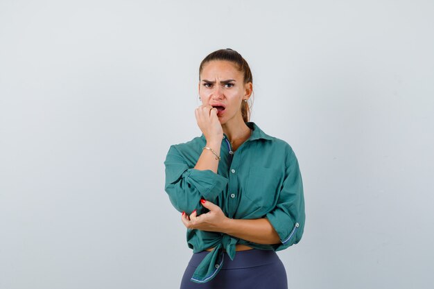 Jonge vrouw die emotioneel nagels bijt in een groen shirt en er verontrust uitziet. vooraanzicht.