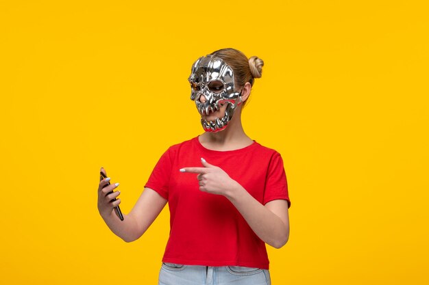 Jonge vrouw die eng gouden masker draagt en haar telefoon gele achtergrond meisjescartoon gebruikt