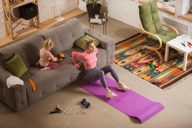 Jonge vrouw die fitness aërobe yoga thuis uitoefent, een sportieve levensstijl die actief wordt terwijl haar kind