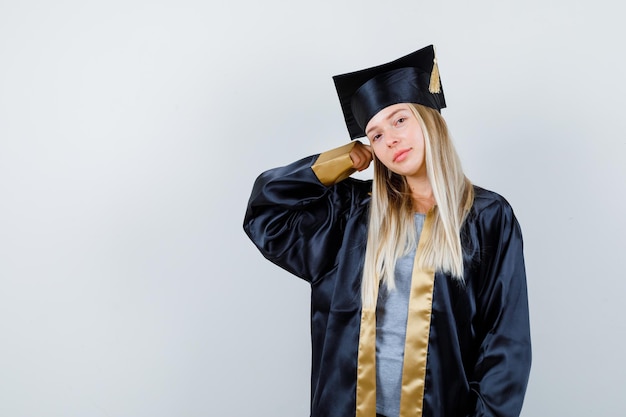 Gratis foto jonge vrouw die gebalde vuist opheft in afgestudeerd uniform en er zelfverzekerd uitziet