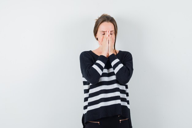 Jonge vrouw die gebedgebaar in gestreepte breigoed en zwarte broek toont en gericht kijkt