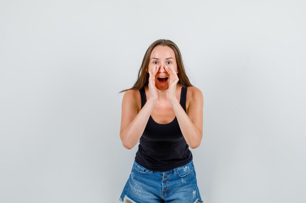 Jonge vrouw die geheim met handen dichtbij mond in hemd, korte broek vertelt