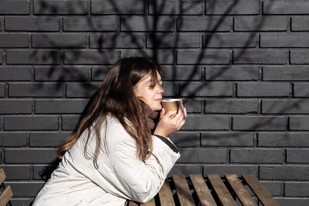 Jonge vrouw die geniet van een drankje tegen de bakstenen muur van de buitenkant van de coffeeshop