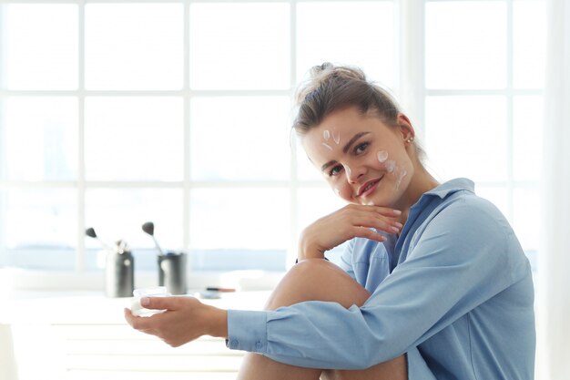 Gratis foto jonge vrouw die gezichtsroom uitspreiden. huidverzorging concept.