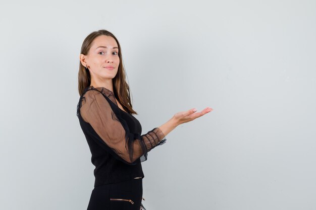 Jonge vrouw die haar hand met open palm opheft die iets in zwarte blouse toont en geconcentreerd kijkt. ruimte voor tekst