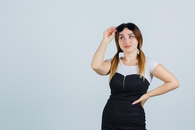 Jonge vrouw die haar hand op een bril houdt terwijl ze haar hand op de heup houdt