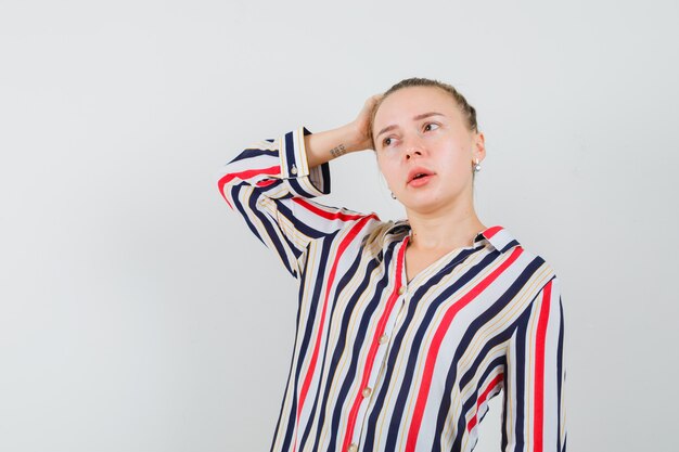 Gratis foto jonge vrouw die haar hand op het hoofd legt en over iets in gestreepte blouse denkt en verward kijkt