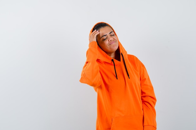 Jonge vrouw die haar hand op het voorhoofd legt, de ogen sluit in een oranje hoodie en er kalm uitziet