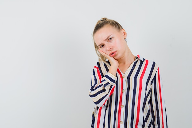 Jonge vrouw die haar hand op wang in gestreepte blouse zet en twijfelachtig kijkt