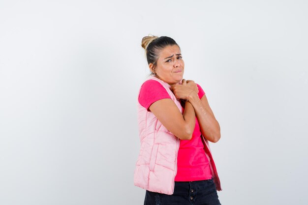 Jonge vrouw die haar handen op de borst rust, rillend in roze t-shirt en jas en er uitgeput uitziet