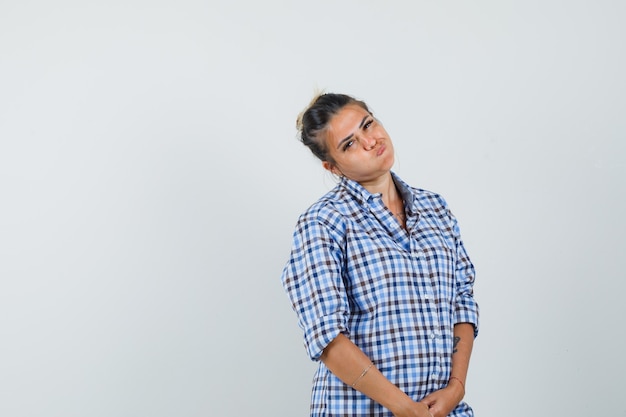 Jonge vrouw die haar lippen in geruit overhemd pruilt en verveeld kijkt.