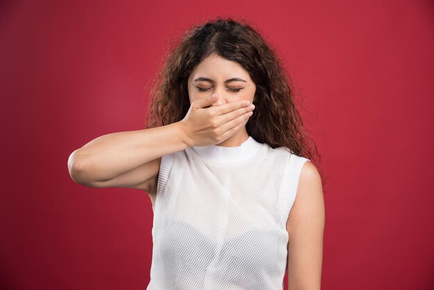 Jonge vrouw die haar mond bedekt met gesloten ogen op een rode