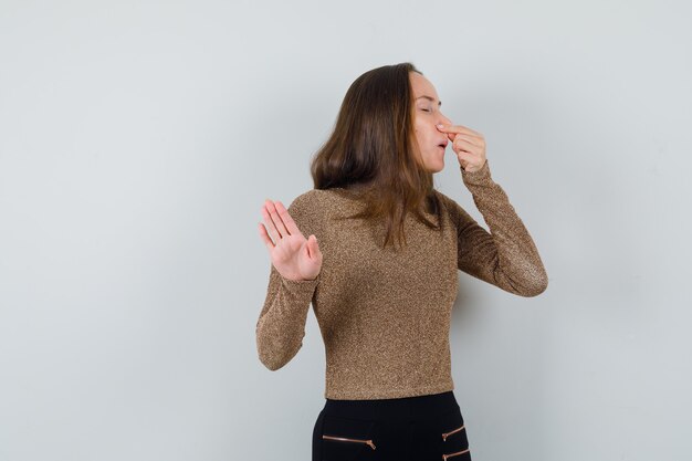 Jonge vrouw die haar neus knijpt terwijl ze iets in gouden blouse afwijst en walgt