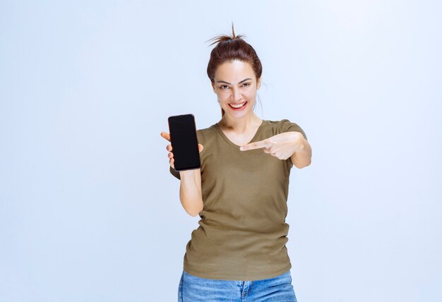 Jonge vrouw die haar nieuwe model zwarte smartphone demonstreert
