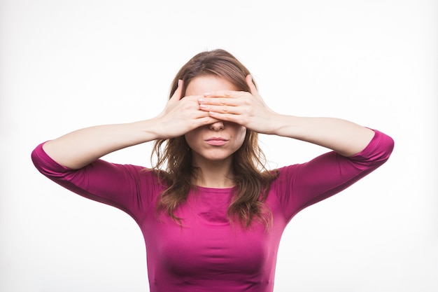 Jonge vrouw die haar ogen met twee handen op witte achtergrond sluit