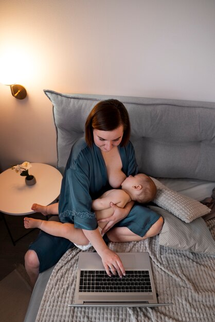 Jonge vrouw die haar schattige baby borstvoeding geeft terwijl ze aan het werk is
