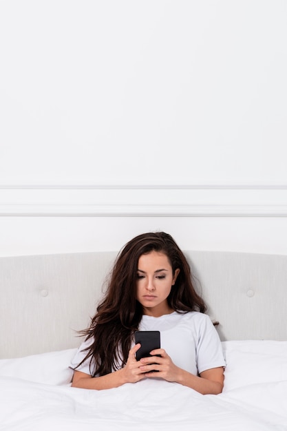 Gratis foto jonge vrouw die haar telefoon in bed controleert