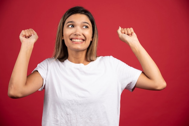 Jonge vrouw die haar vuisten opheft omhoog op rode muur.