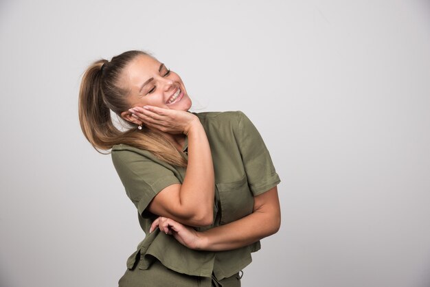 Jonge vrouw die haar wang op grijze muur houdt.