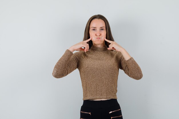 Jonge vrouw die haar wangen in gouden blouse knijpt