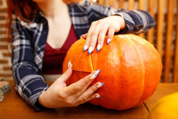 Jonge vrouw die halloween-pompoen jack-o-lantern maakt. vrouwelijke handen snijden pompoenen met mes.