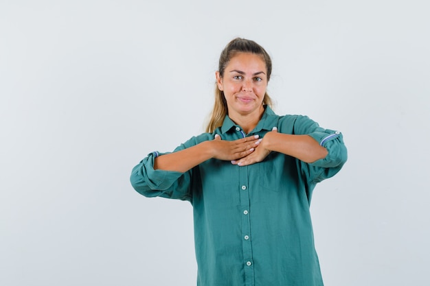 Jonge vrouw die hand op borst in groene blouse rust en gelukkig kijkt